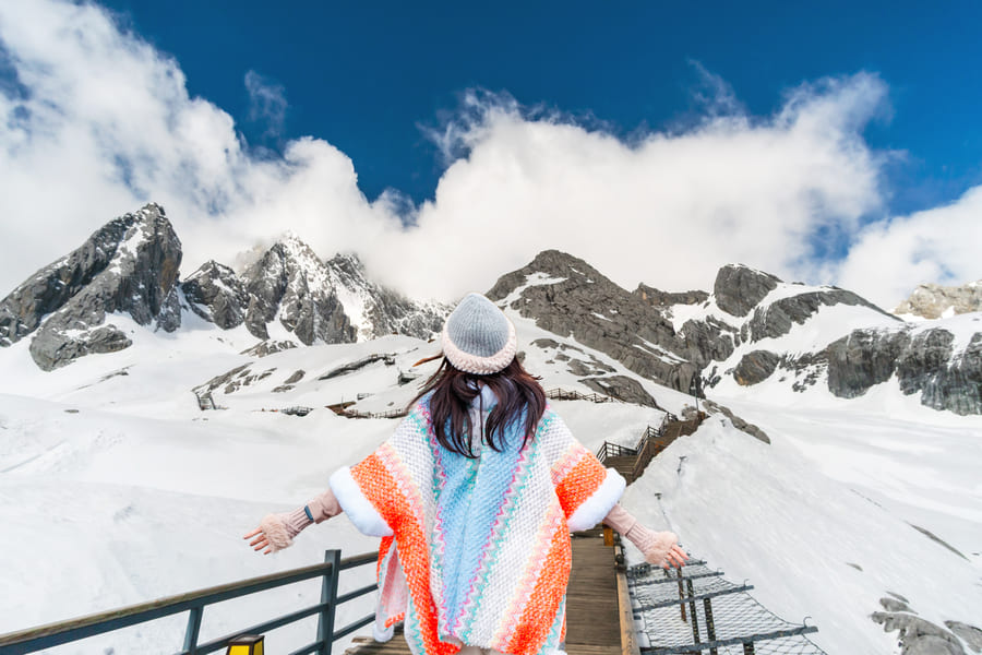 una mujer parada en un mirador con los brazos extendidos admirando unas montañas cubiertas de nieve