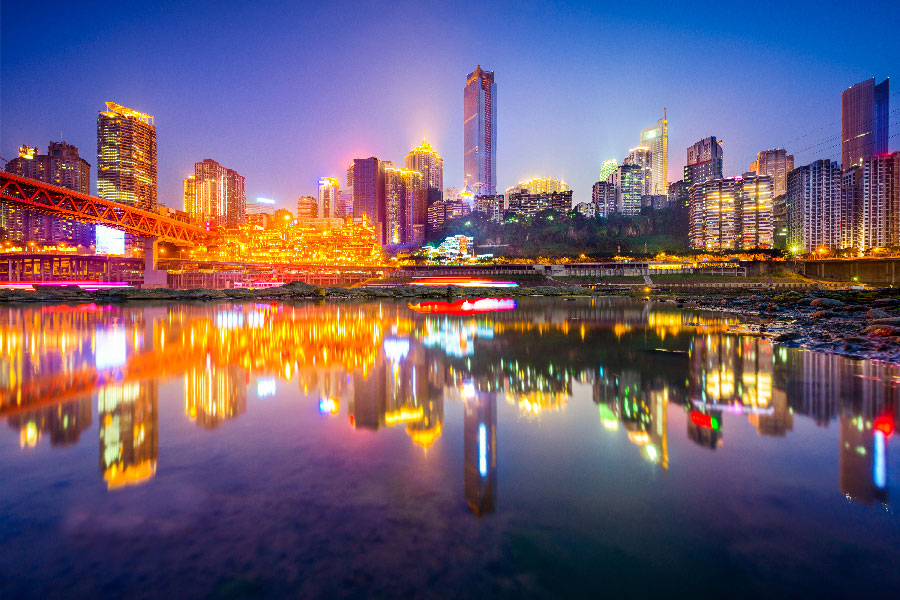 una gran ciudad de noche muy colorida por las luces que se ve reflejada sobre un lago